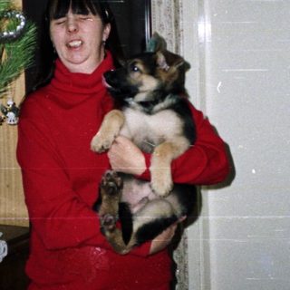 Woman holds a puppy near a decorated Christmas tree.