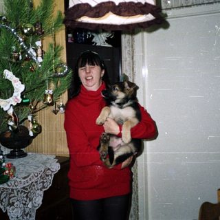 Woman holds a puppy near a decorated Christmas tree.