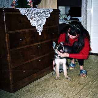Woman kneeling, holding a puppy in a tiled room.