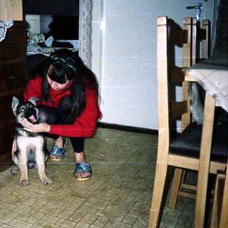 Woman kneeling, holding a puppy in a tiled room.