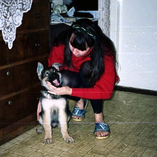 Woman kneeling, holding a puppy in a tiled room.