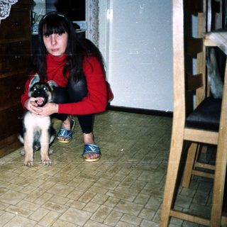 Woman crouches near a puppy in a tiled room.