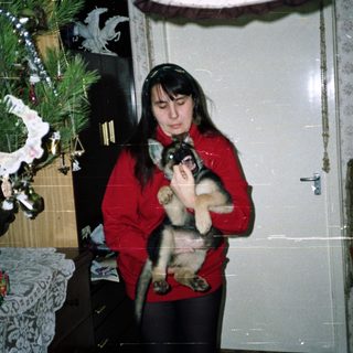 Woman holds cat indoors near a Christmas tree.