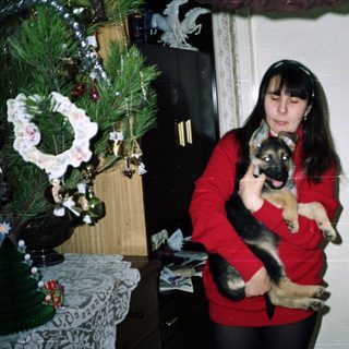 Woman holds German Shepherd puppy near a decorated Christmas tree.