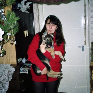 Woman holds German Shepherd puppy near a decorated Christmas tree.