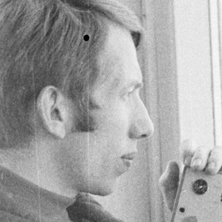 Man in jacket takes a picture near a window.