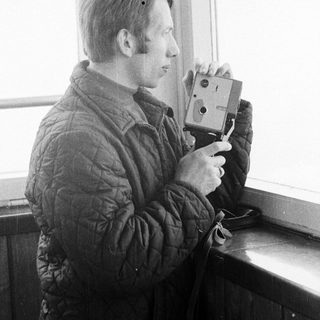 Man in jacket takes a picture near a window.