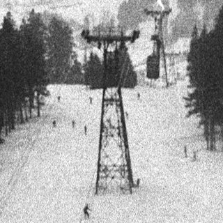 Ski lift ascends a snowy slope with forested mountains.