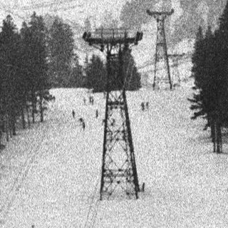 Ski lift ascends a snowy mountainside with forested slopes.