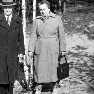 Couple stands near a tree in a wooded area.