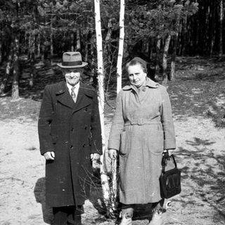 Couple stands near a tree in a wooded area.
