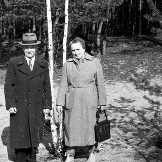 Couple stands near a tree in a wooded area.