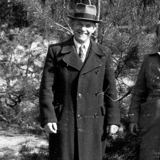 Couple stands outdoors in coats, posing in a wooded area.