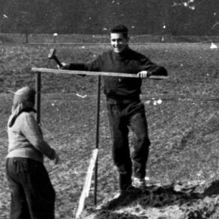 Two figures standing near a pile of dirt in a field.