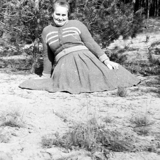 Woman in dress lies on sandy ground near trees.