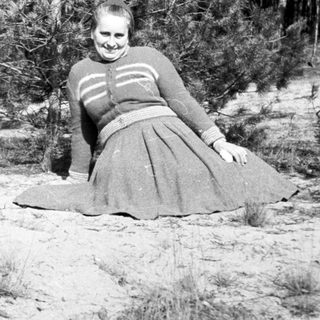 Woman in dress lies on sandy ground near trees.