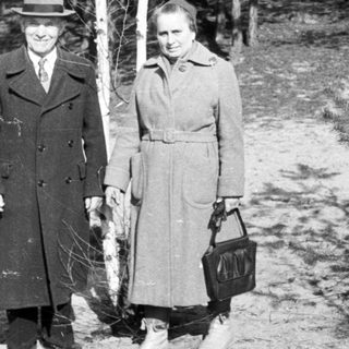 Man and woman stand near a tree in a wooded area.