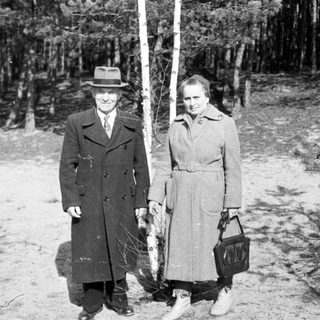 Man and woman stand near a tree in a wooded area.
