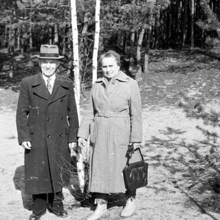 Man and woman stand near a tree in a wooded area.