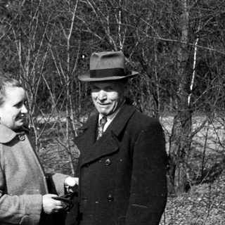 Couple stands in a sparse, wooded area.