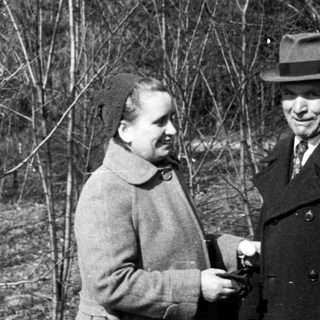 Couple stands in a sparse, wooded area.