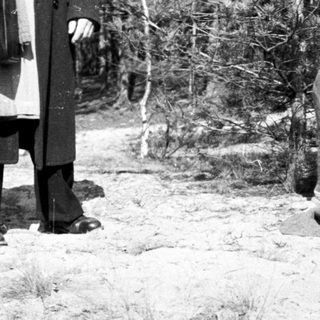 Woman kneeling in a field, with a person nearby.