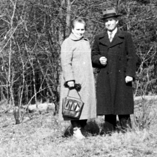 Here's a brief summary of the image: Couple stands in a grassy, wooded area.