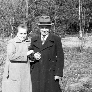 Couple stands outdoors in a wooded area.