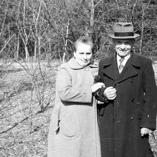 Couple stands outdoors in a wooded area.