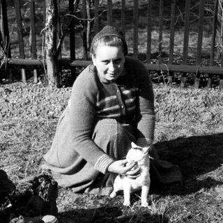 Woman sits outdoors with a small kitten in her lap.