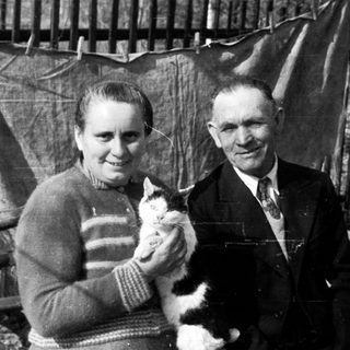 Black and white photo shows a couple holding a cat.