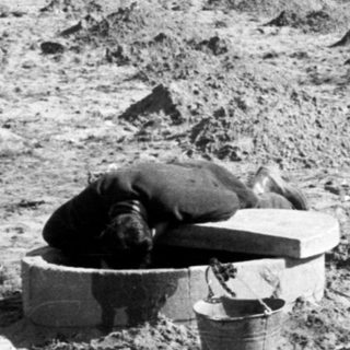 Man rests in excavated ground with buildings in background.