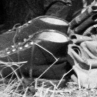 Woman sits outdoors with belongings, appearing to rest.