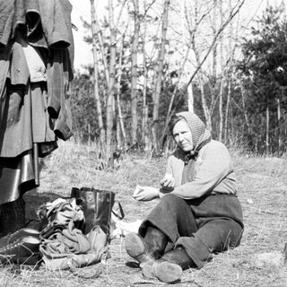 Woman sits outdoors with belongings, appearing to rest.