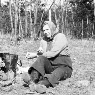 Woman sits outdoors with belongings, appearing to rest.