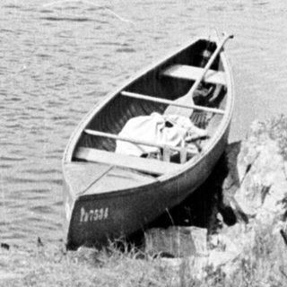 Here's a brief summary of the image: Boats rest on a shore with a lake and hillside.