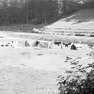 Black and white image of a riverside campsite with tents.