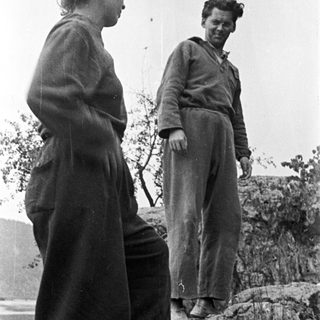 Two people stand on a rocky hillside, looking out.