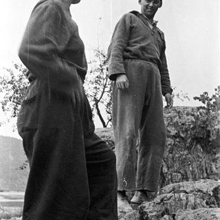 Two people stand on a rocky hillside, looking out.