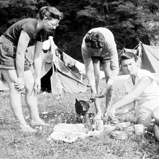 Three people camping and preparing food outdoors.