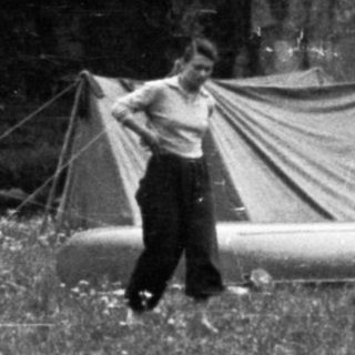 Here's a brief summary of the image: Tents, laundry, and people in a grassy, wooded area.