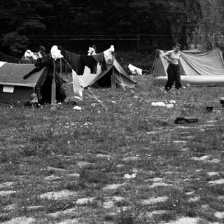 Here's a brief summary of the image: Tents, laundry, and people in a grassy, wooded area.