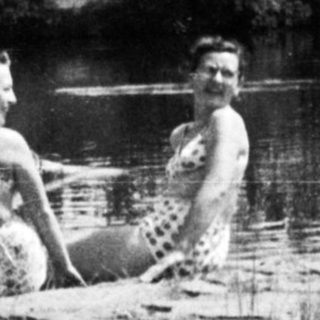 Two women sit on a log in a rushing stream.