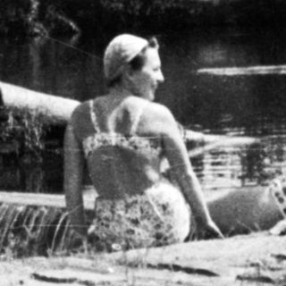 Two women sit on a log in a rushing stream.