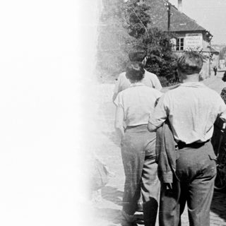 Here's a brief summary of the image: Group of men walking down a street, viewed from behind.
