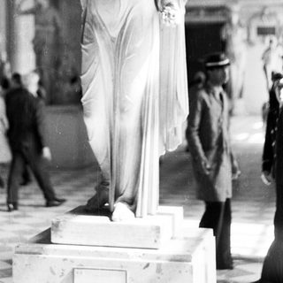 Marble statue displayed in a museum, people observing.