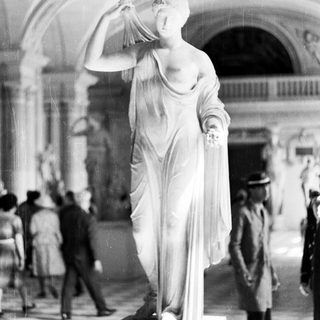 Marble statue displayed in a museum, people observing.