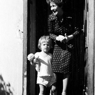 Child and woman stand on a doorstep.