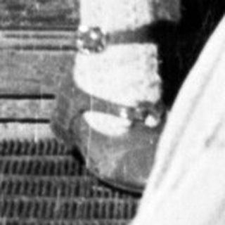 Here's a brief summary of the image: Baby stands outside a door, holding a toy.