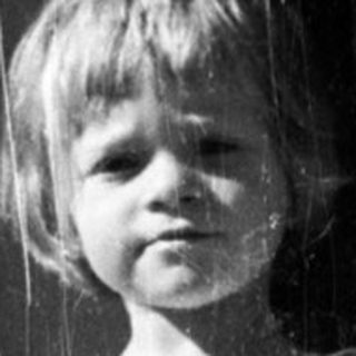 Here's a brief summary of the image: Child stands in a doorway, holding an object.